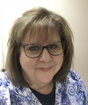 Veterinary staff member with glasses smiling in a blue and white scrub top.